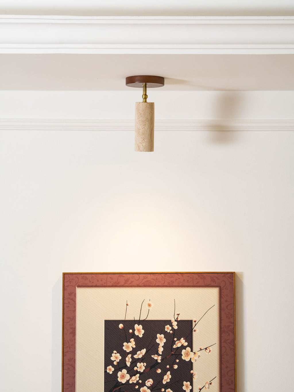 Clérachic travertine spotlight on the ceiling above a large framed blossom print, with a soft pool of light on the white wall.