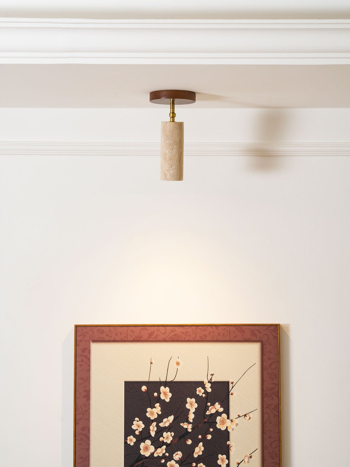 Clérachic travertine spotlight on the ceiling above a large framed blossom print, with a soft pool of light on the white wall.