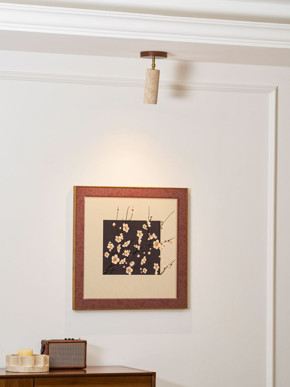 Clérachic spotlight on a white ceiling pointing at a framed blossom print, with a small speaker and a candle on a sideboard below.
