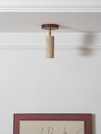 Clérachic travertine spotlight hanging straight down from a white ceiling by a cornice, with the top of a picture frame below.