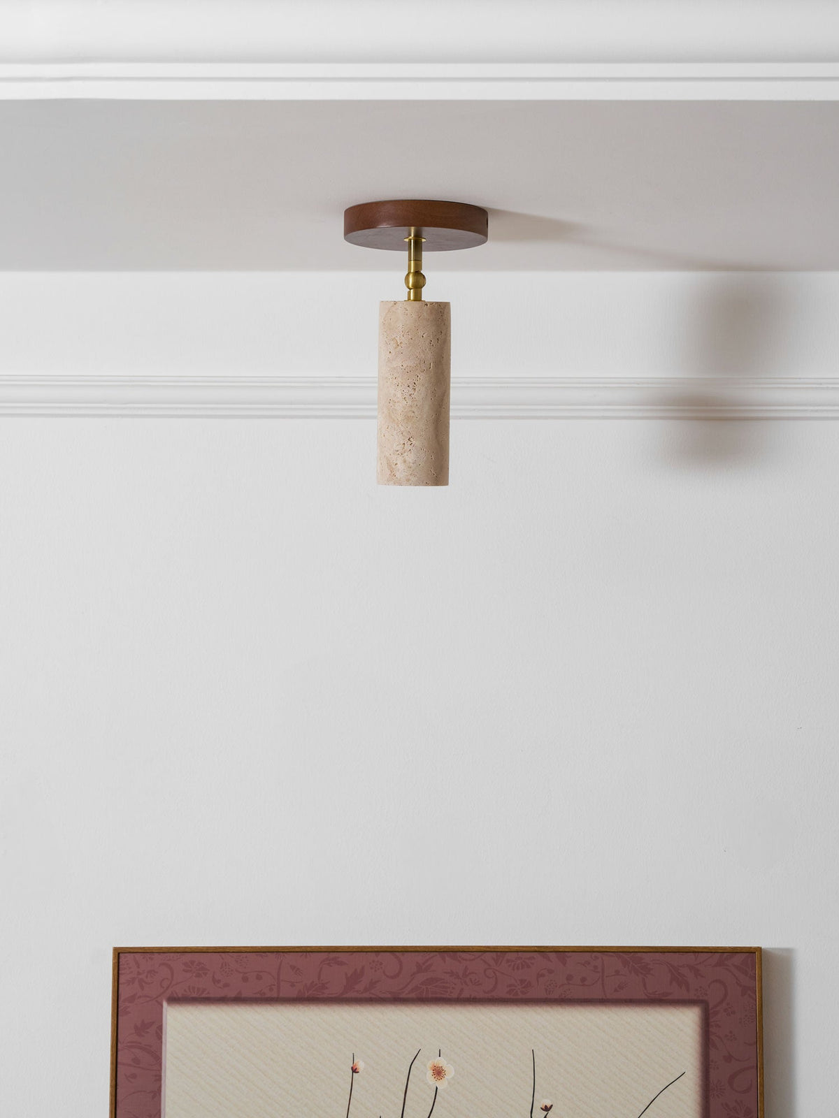 Clérachic travertine spotlight hanging straight down from a white ceiling by a cornice, with the top of a picture frame below.