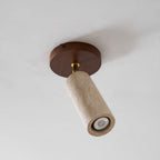 Underside view of the Clérachic travertine cylinder and its round walnut ceiling plate, with a small bulb visible in the open end.