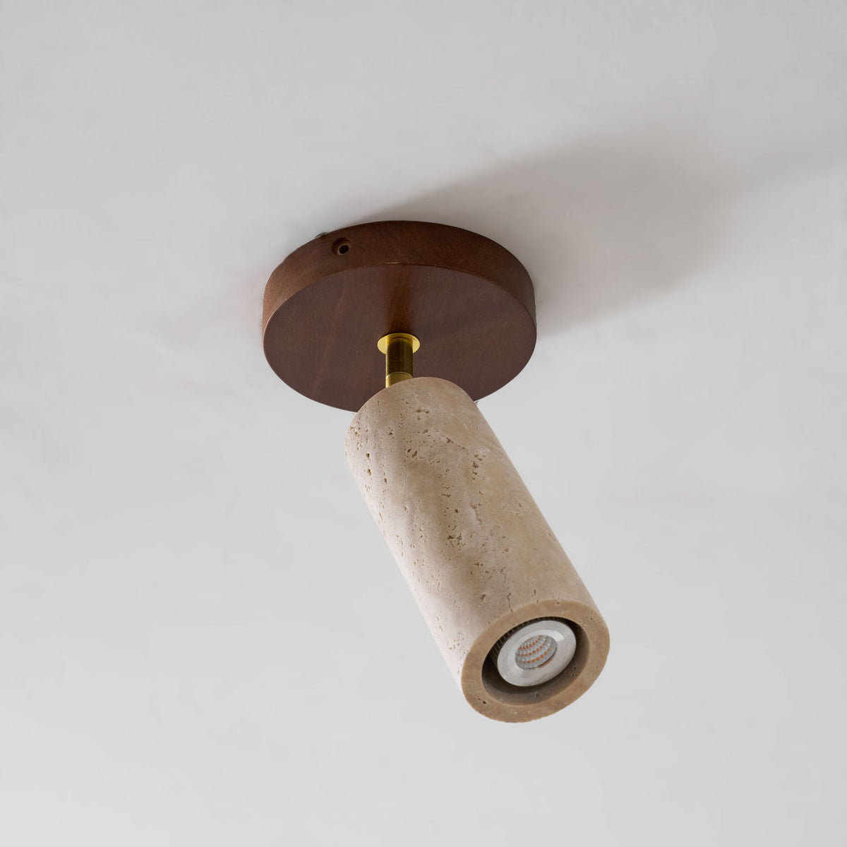 Underside view of the Clérachic travertine cylinder and its round walnut ceiling plate, with a small bulb visible in the open end.