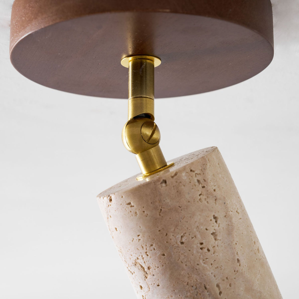 Close view of the walnut ceiling plate and brass swivel joint of this Clérachic spotlight, with the top of the travertine cylinder below.