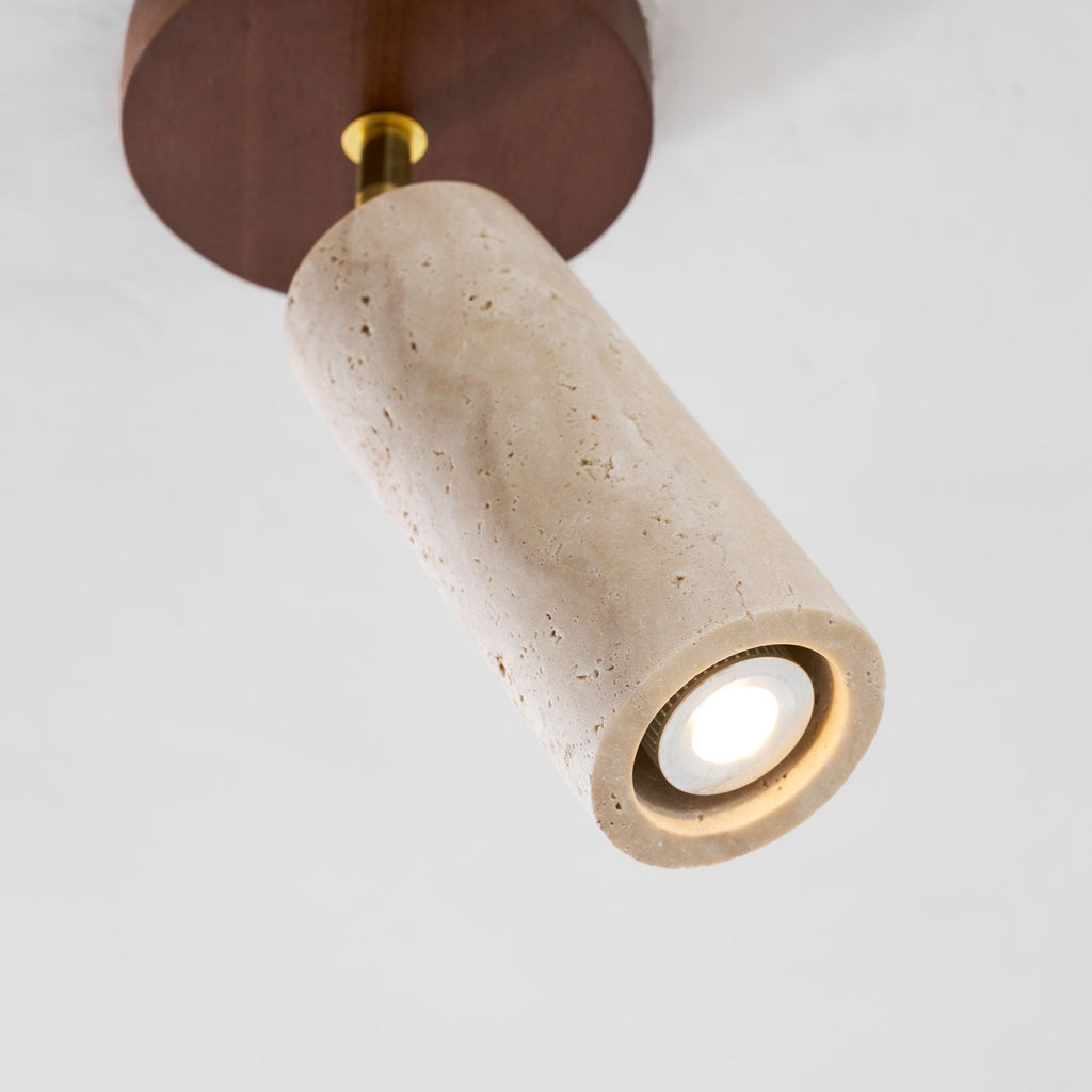 Angled close view of this Clérachic travertine spotlight, its pitted stone cylinder tipped down with a bright small lamp in the end.