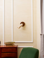 Small Clérachic travertine spotlight fitted to a cream panelled wall above a walnut cabinet with a stack of books and a green chair.
