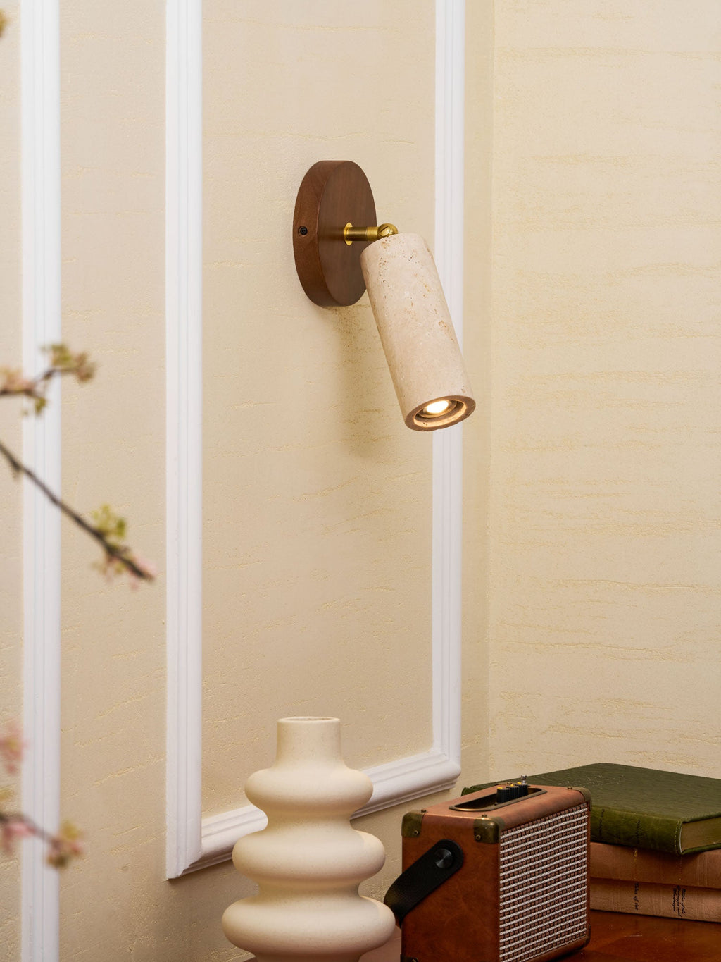 Clérachic travertine spotlight on a round walnut wall plate, angled to the right, with a cream vase and a speaker on a shelf below.