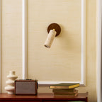 Clérachic spotlight tilted down on a cream wall with white moulding, above a walnut sideboard with a vase, a speaker and books.