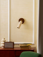 Smaller view of the wall-mounted Clérachic travertine spotlight on a cream panelled wall above a speaker, a vase and a green chair.