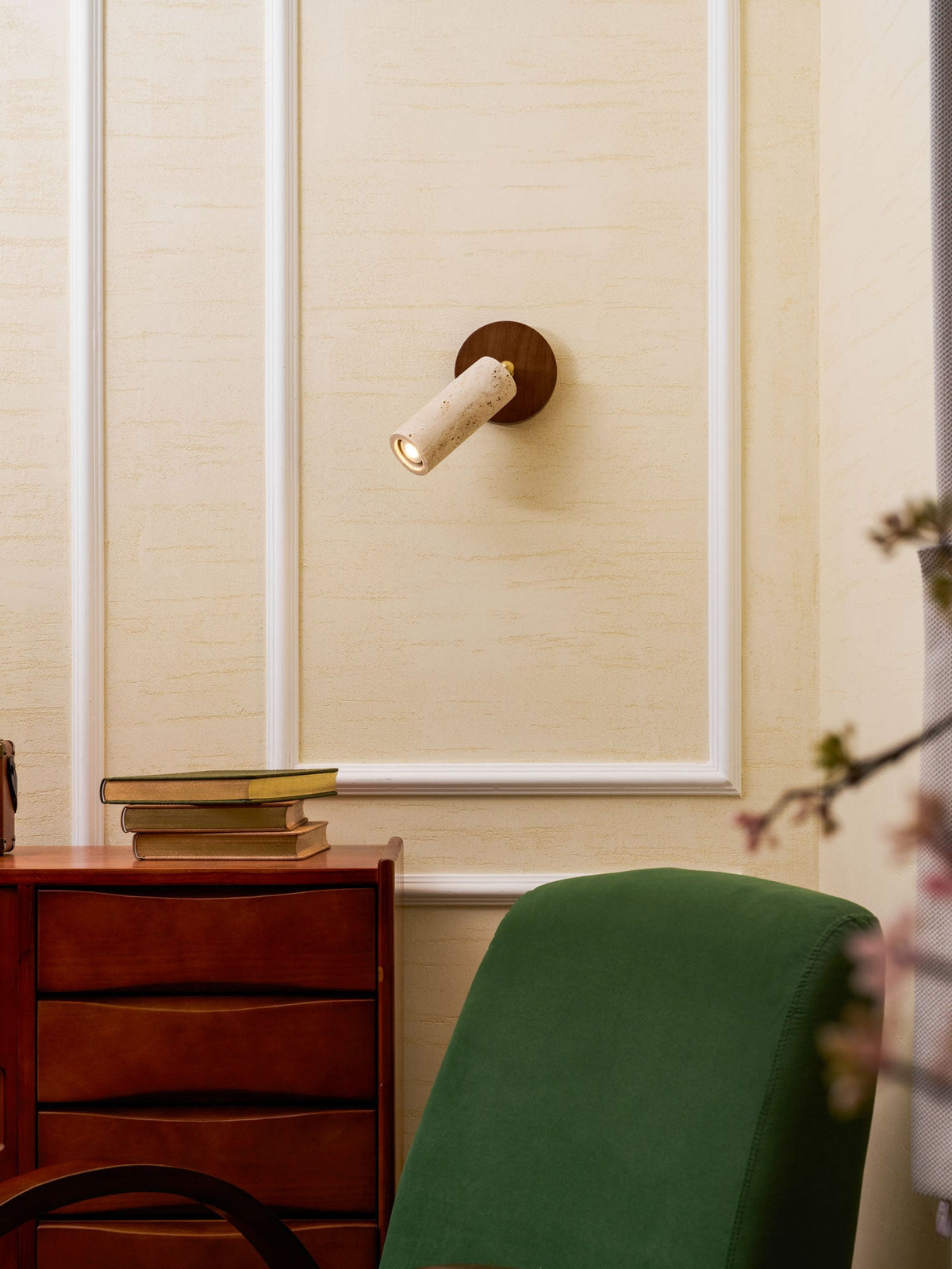 Clérachic travertine wall spotlight with the cylinder turned to the left, above a walnut chest of drawers and a green chair.