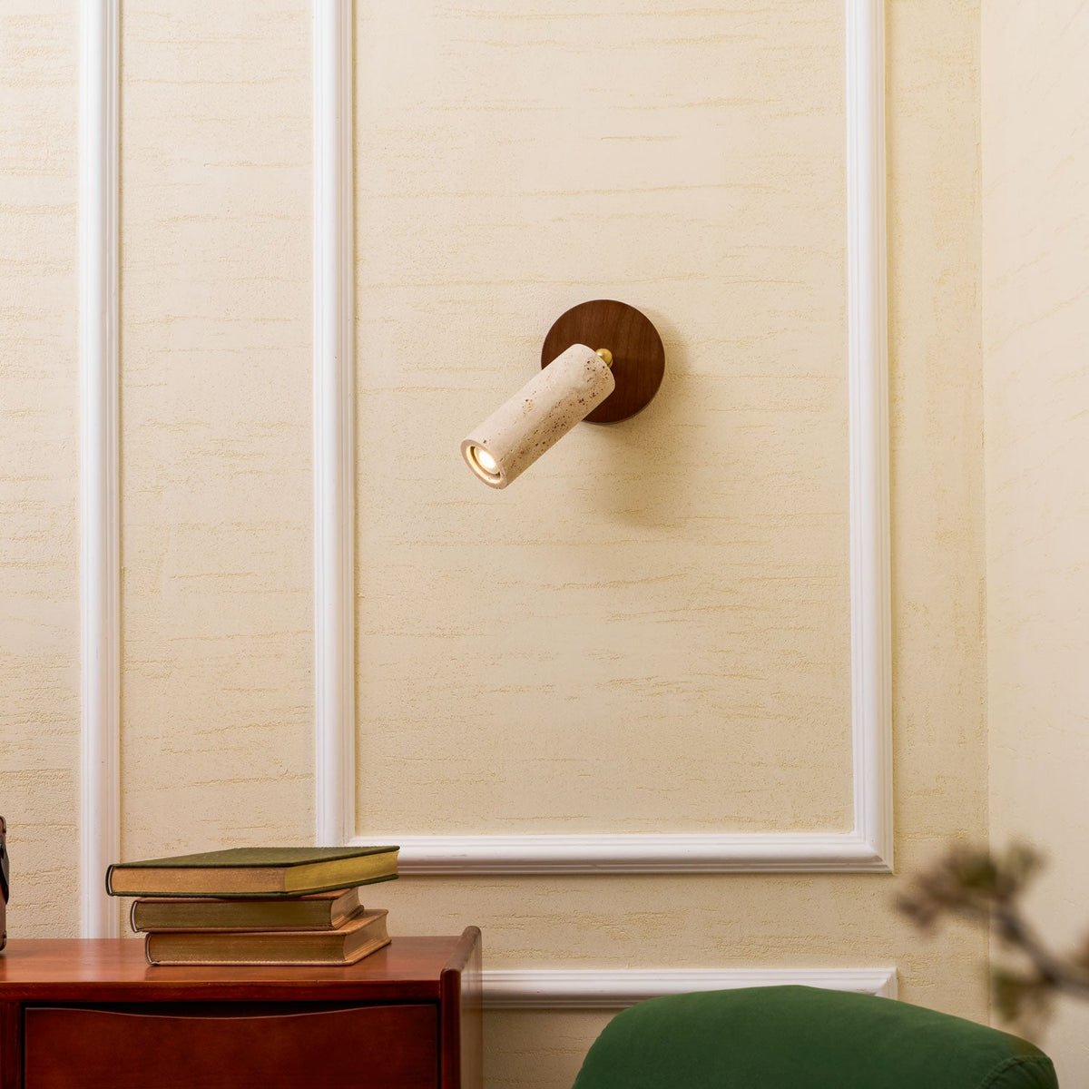 Clérachic wall spotlight angled left on a walnut plate, on a cream wall with white moulding and a stack of books at the bottom.
