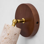 Close view of the round walnut wall plate and brass swivel joint of this Clérachic spotlight, with a travertine cylinder beneath.