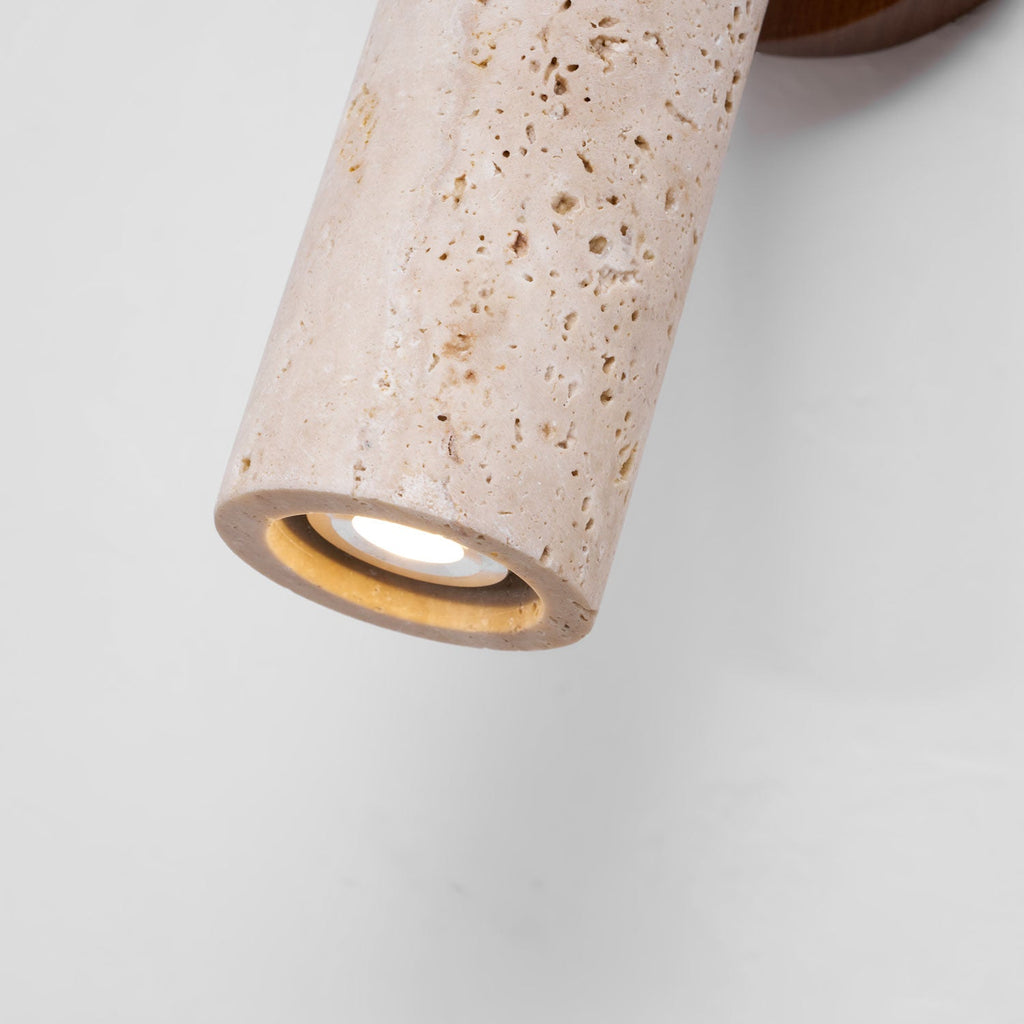 Close view of the open end of the Clérachic travertine cylinder, its pitted stone surface and a small bulb inside, against a white wall.