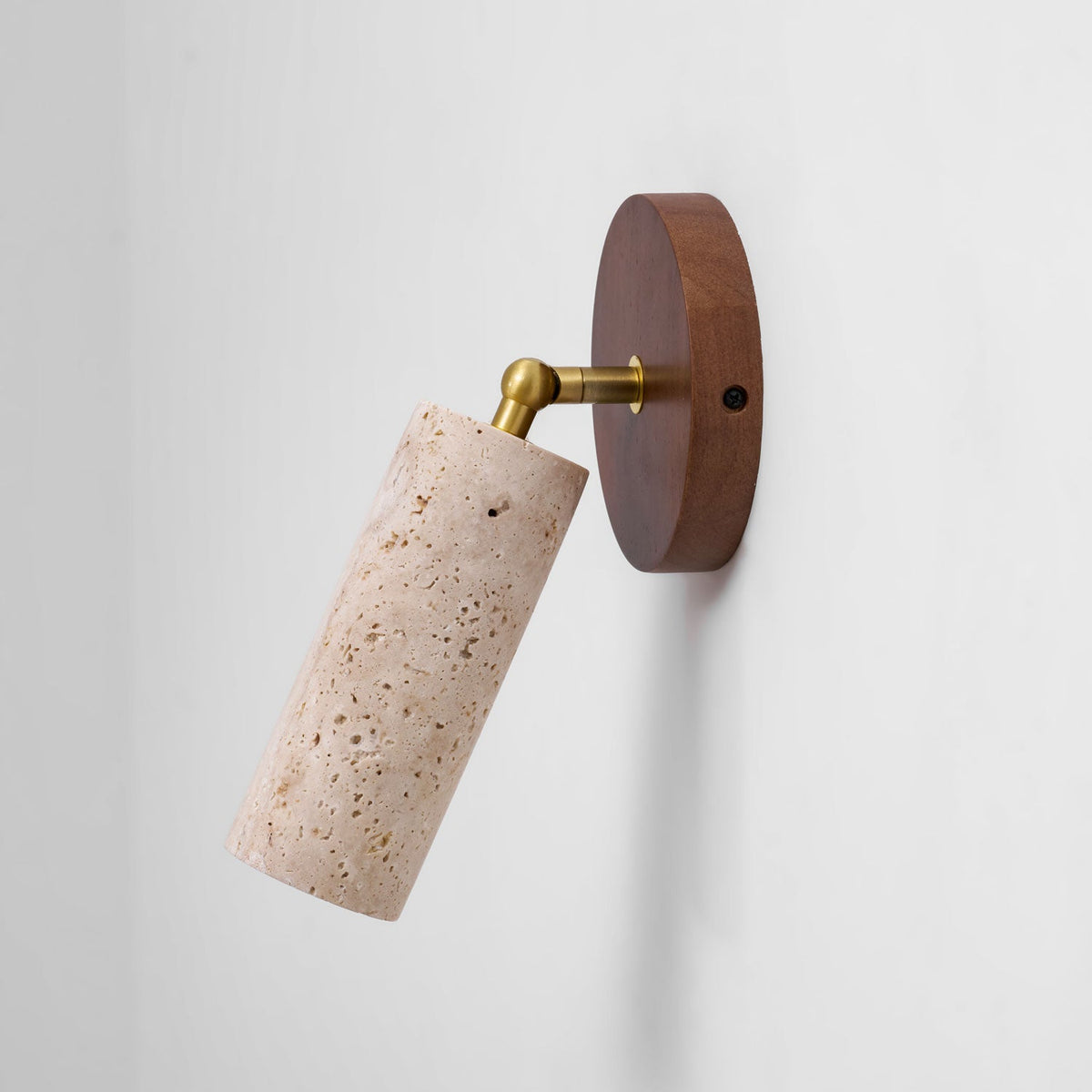 Clérachic travertine spotlight swung out to one side on its brass joint from a walnut wall plate, on a plain white wall.