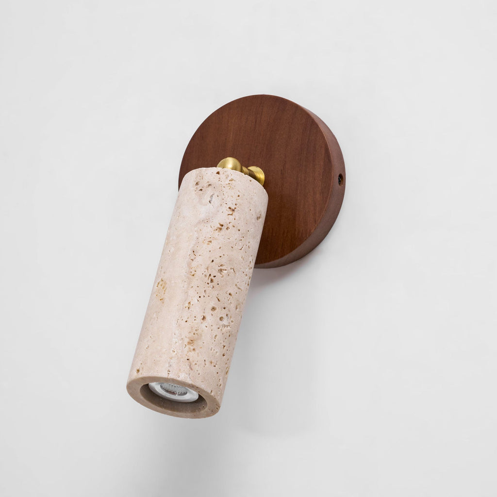 Clérachic travertine spotlight tilted on a round walnut wall plate against a pale background, with the small bulb visible in the open end.