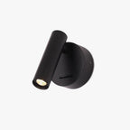 A Clérachic spotlight wall light in black, with a round backplate, a slim cylinder head angled down and a small slide switch, on white.