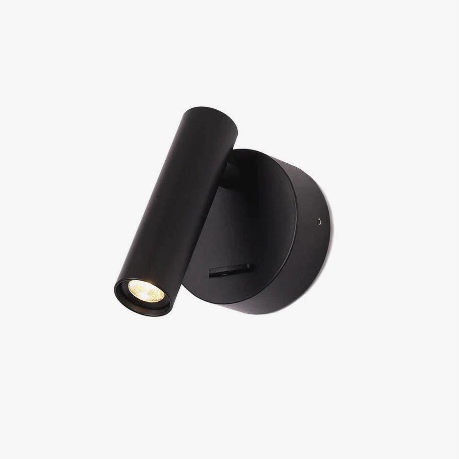 A Clérachic spotlight wall light in black, with a round backplate, a slim cylinder head angled down and a small slide switch, on white.