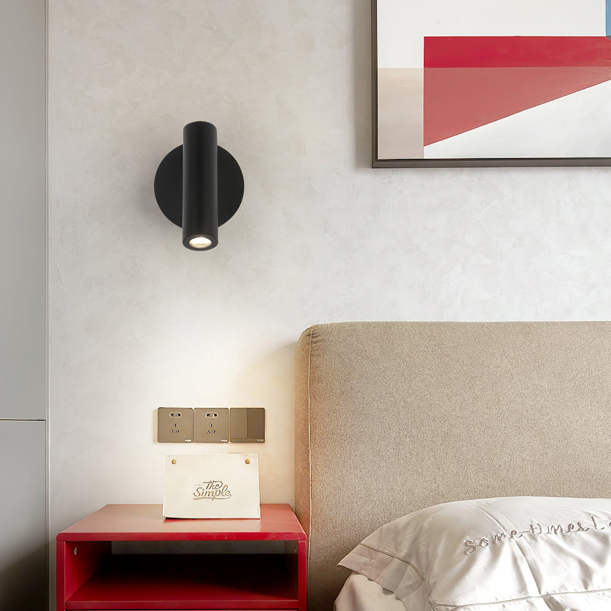 A black Clérachic spotlight wall light above a red bedside shelf and a beige headboard, with art in the top corner of the frame.