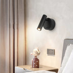This Clérachic wall light, black with a short round backplate, sits beside floor-length curtains above a bedside table with a small figurine.