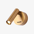 Copper-toned Clérachic spotlight wall light, lit, with a round backplate and a slide switch below the cylinder head, on a white backdrop.