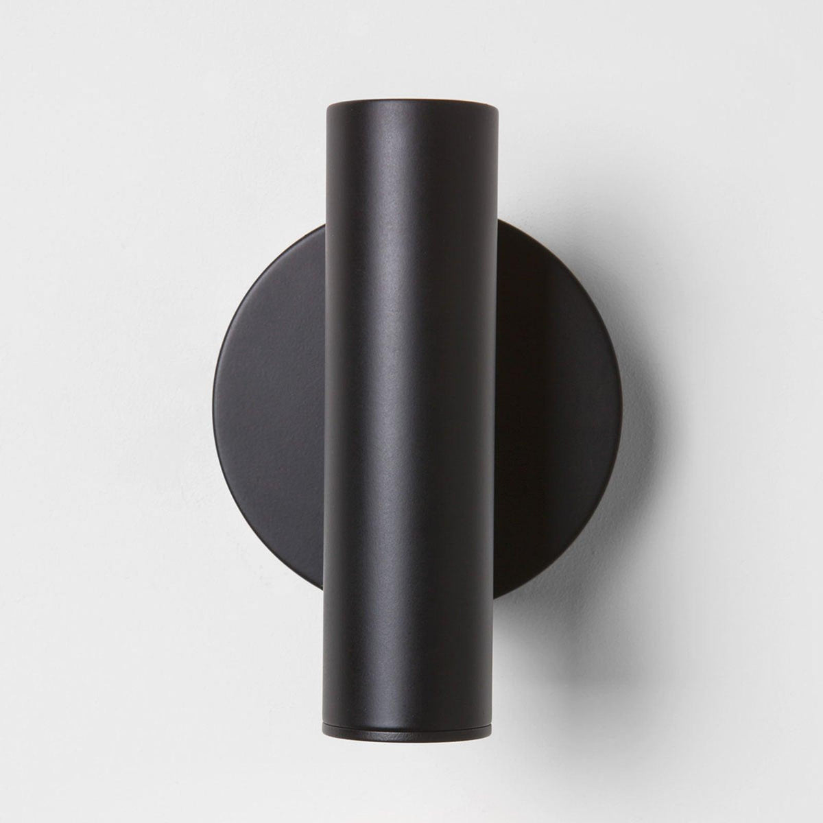 Front view of this Clérachic wall light in black, showing the cylinder head standing upright over a round backplate on a white wall.
