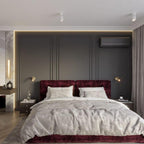 Two small gold-toned Clérachic wall lights sit on either side of a dark panelled headboard wall, above a bed with a burgundy headboard.