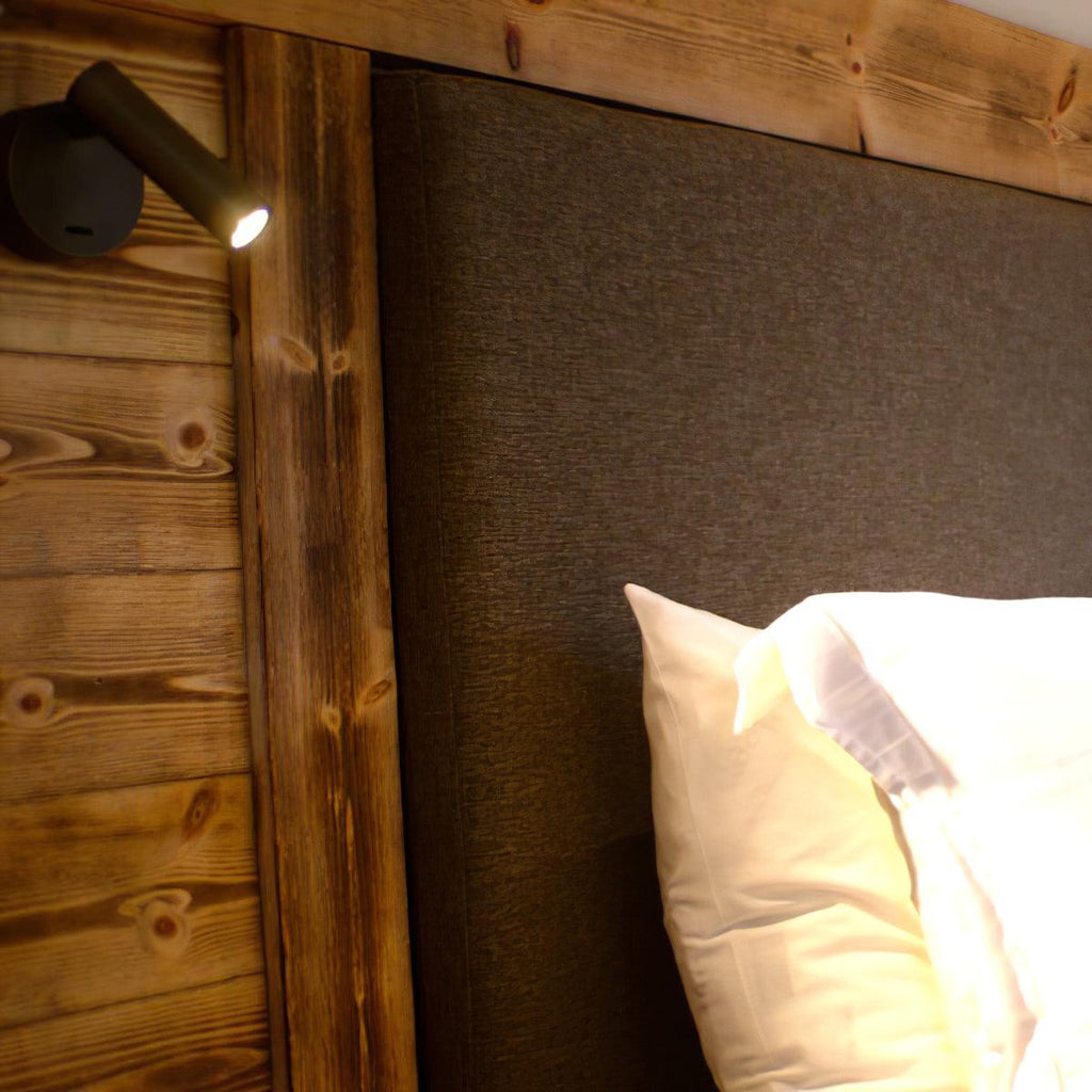 Close view of this Clérachic spotlight wall light on a wood-plank headboard, its small head lit and angled toward the pillows.