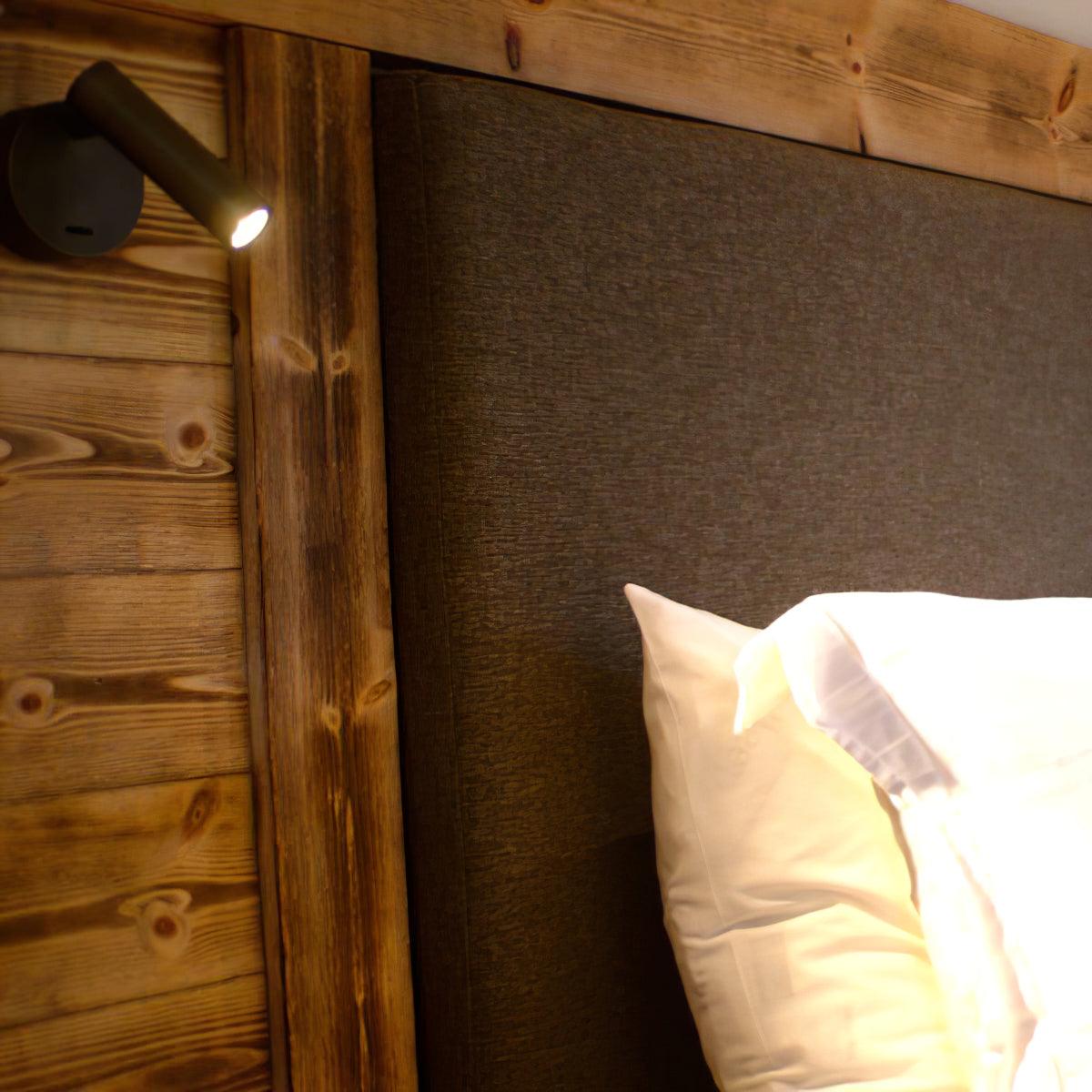 Close view of this Clérachic spotlight wall light on a wood-plank headboard, its small head lit and angled toward the pillows.