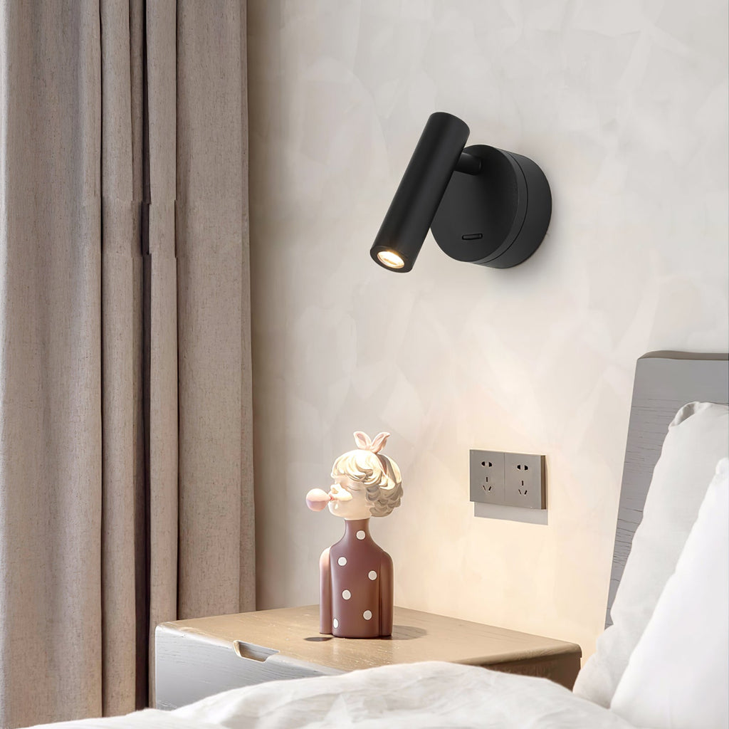 A black Clérachic reading light on a cream wall beside curtains, above a bedside table with a figurine and a bed pillow.