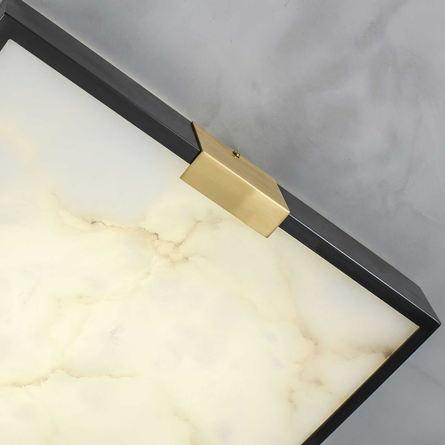 Corner detail of the Clérachic Square Alabaster Flush Mount Ceiling Light, the alabaster faintly lit so fine veining shows beneath the brass saddle.