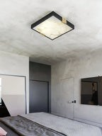Clérachic Square Alabaster Flush Mount Ceiling Light lit in a concrete-walled bedroom, the veined stone panel glowing warm against raw grey plaster.