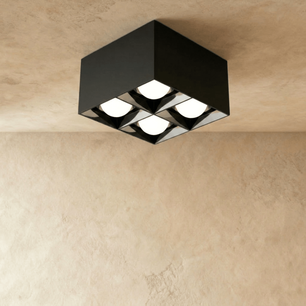 Clérachic black square box ceiling downlight with four round lit spot cells, fixed to a ceiling above a limewash wall in the studio.