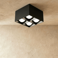 Clérachic black square box ceiling downlight with four round lit spot cells, fixed to a ceiling above a limewash wall in the studio.