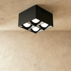 Clérachic black square box ceiling downlight with four round lit spot cells, fixed to a ceiling above a limewash wall in the studio.