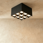Clérachic black square box ceiling downlight with nine lit spot cells in a three by three grid, studio shot on limewash.