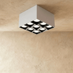 Clérachic white square box ceiling downlight with nine lit spot cells and black inner reflectors, shown in the studio on limewash.