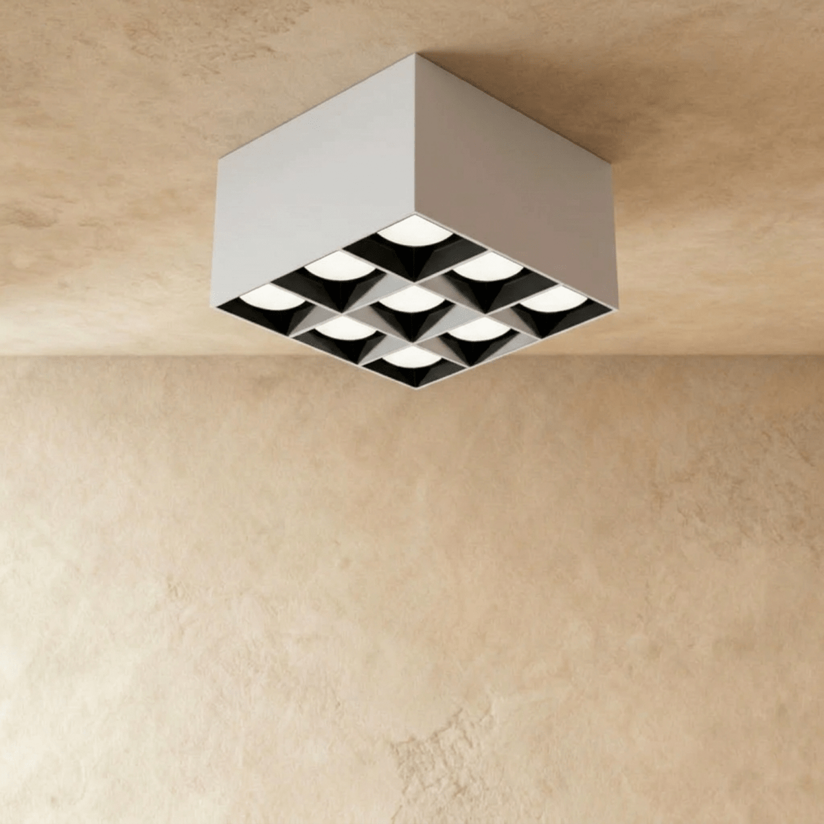 Clérachic white square box ceiling downlight with nine lit spot cells and black inner reflectors, shown in the studio on limewash.