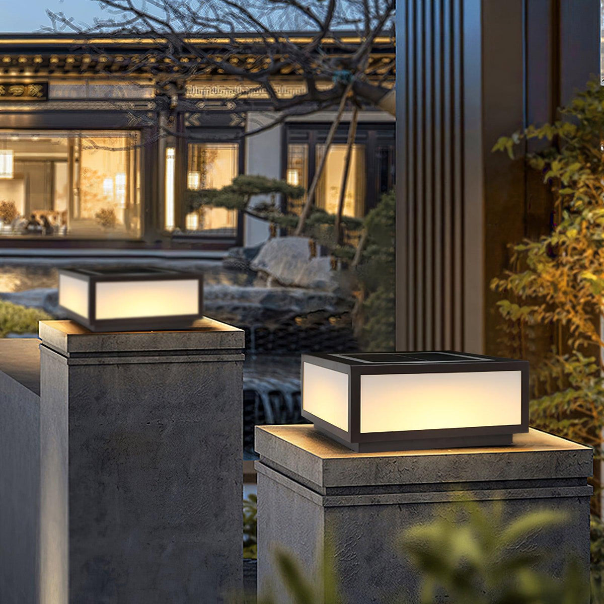 Two lit square post lights from Clérachic on stone gate pillars, with a softly lit courtyard house in the background at dusk.