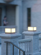 Close view of two lit Clérachic post lights on brick pillars, with a stone balustrade and a handrail beside the steps.