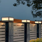 Row of lit square Clérachic post lights along slatted fence pillars, seen against a twilight sky and a timber pergola.
