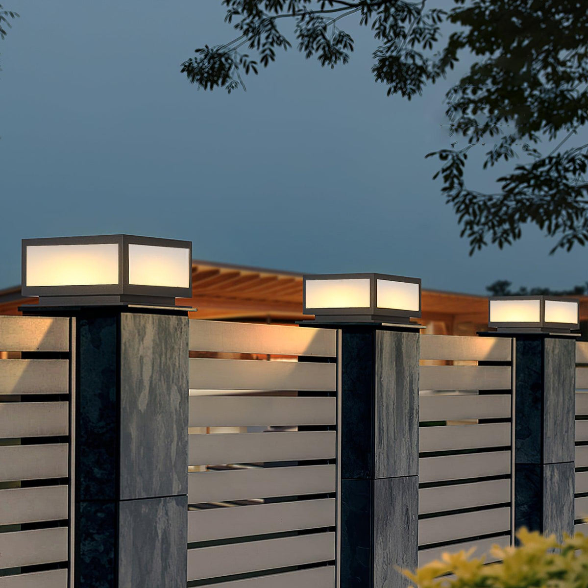 Row of lit square Clérachic post lights along slatted fence pillars, seen against a twilight sky and a timber pergola.