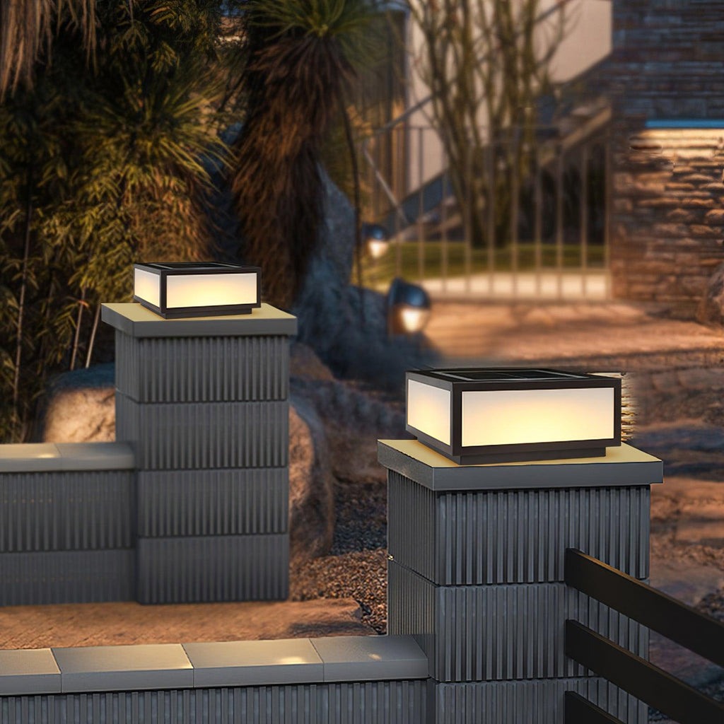 Two Clérachic post lights glowing on ribbed grey pillars in a garden at night, with palms and a path lit behind them.