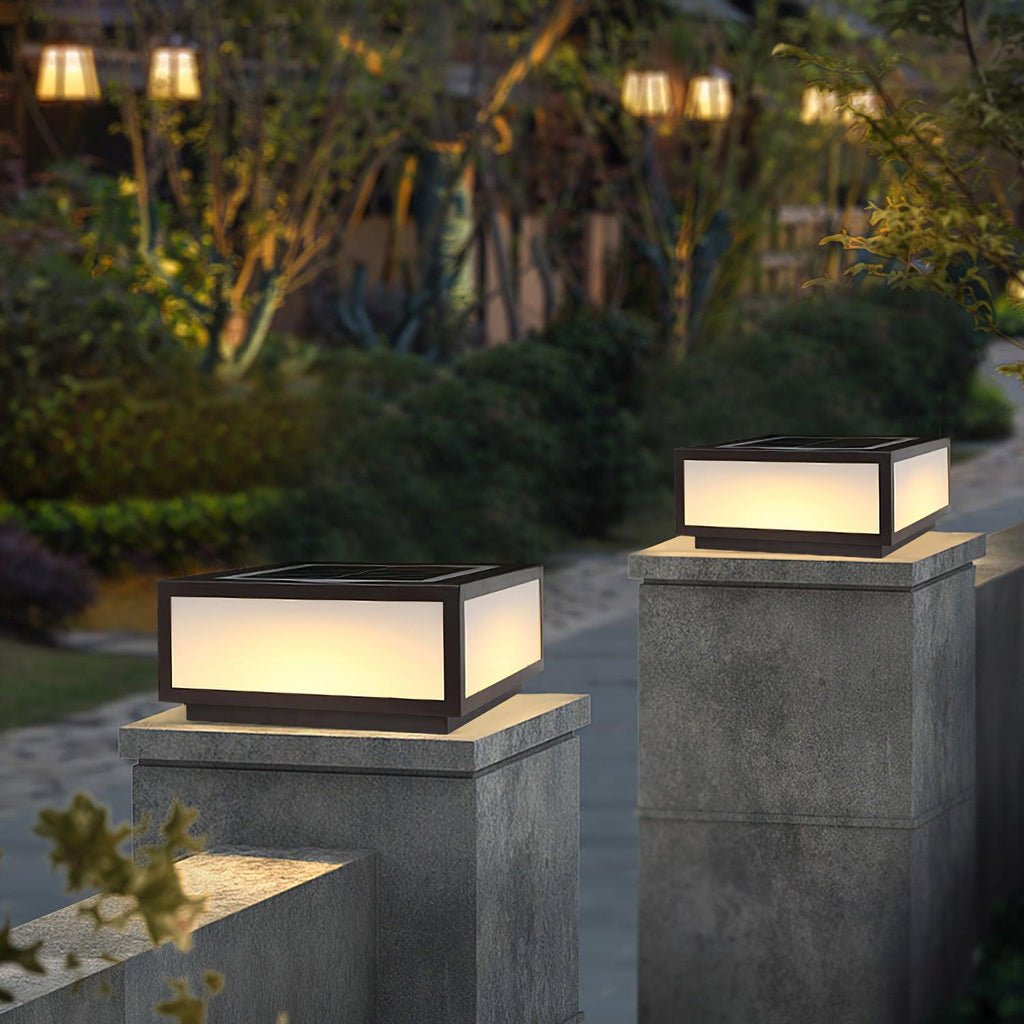 Frosted white panels glowing warm on a Clérachic square post light on a concrete pillar, with garden planting around it at dusk.