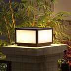 Lit Clérachic square post light on a tiled pillar, surrounded by bamboo leaves, with a soft glow under its base.