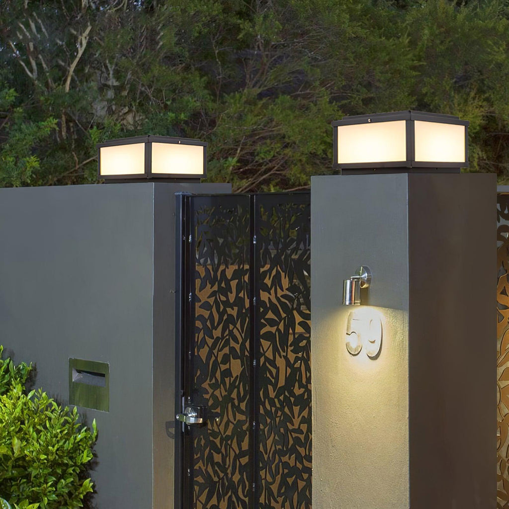 Two lit Clérachic post lights on dark gate pillars either side of a leaf-pattern metal gate and a house number light.