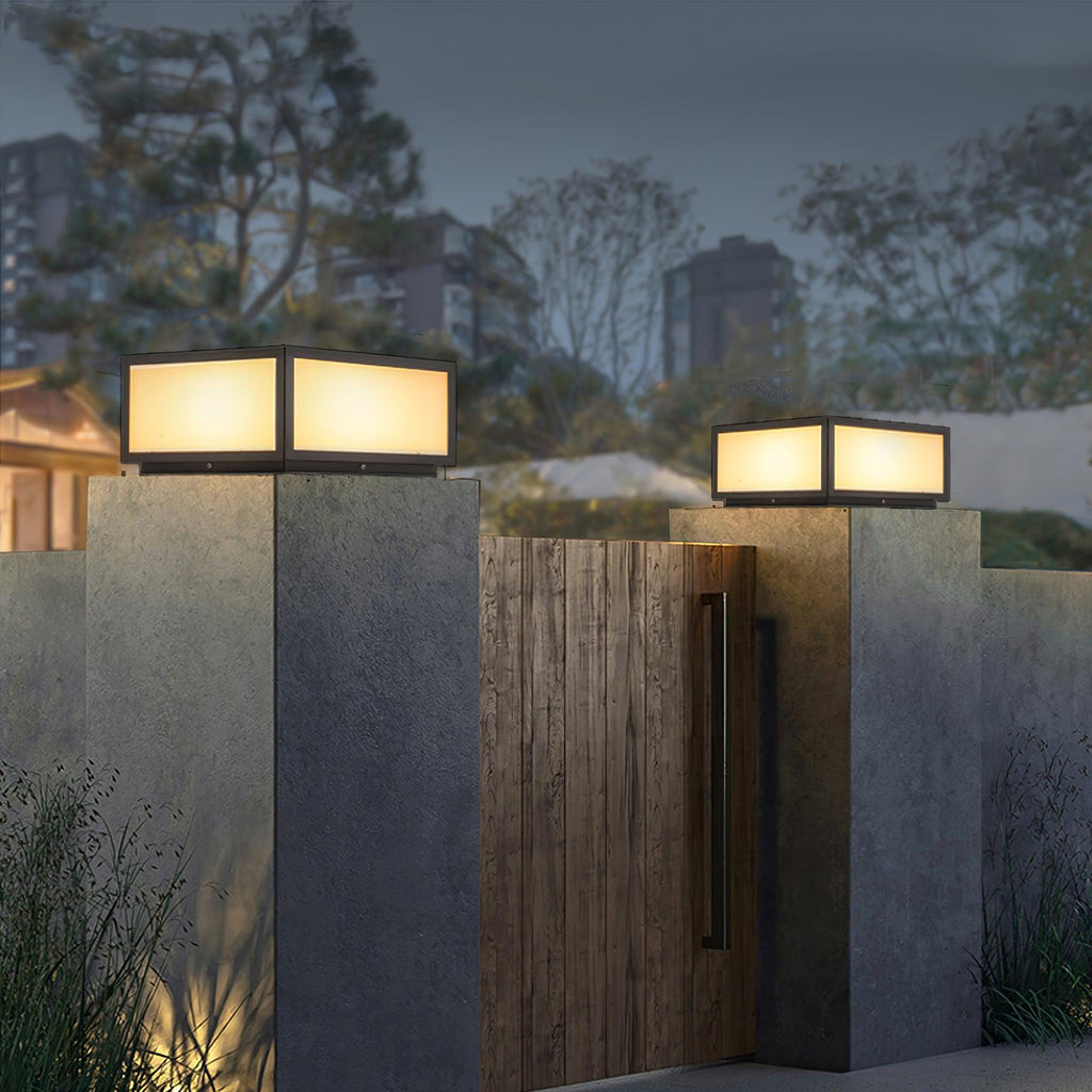 Clérachic post lights glowing on grey concrete pillars either side of a timber gate, with city lights in the distance.