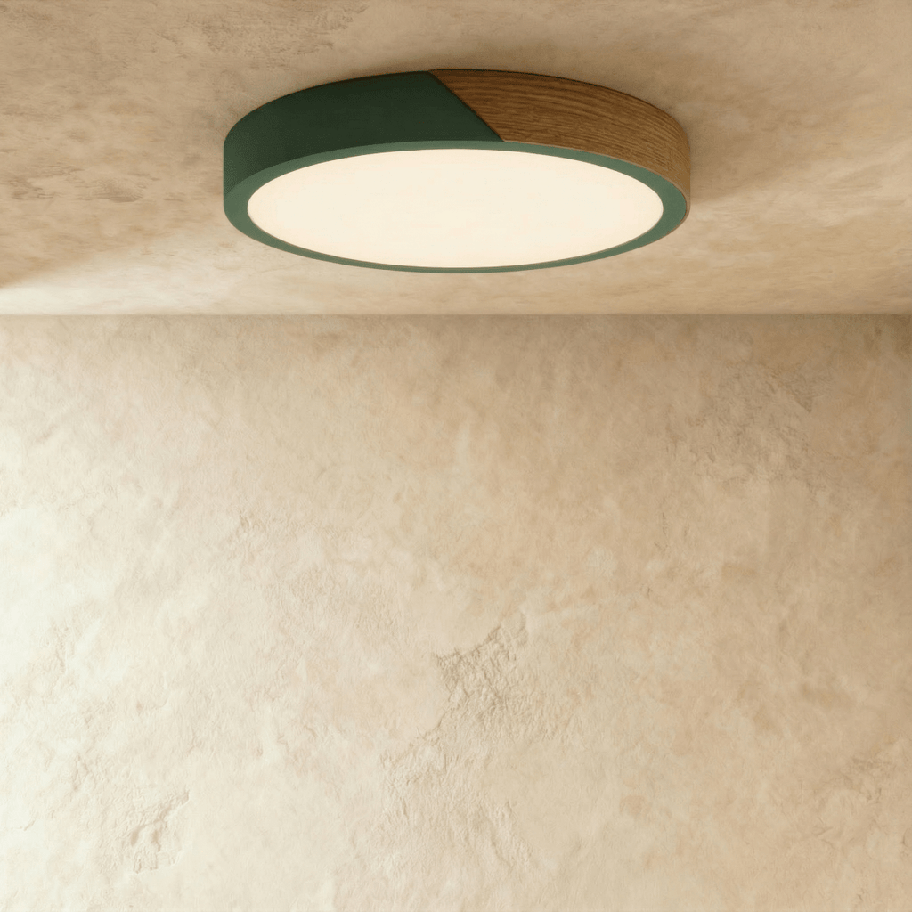 Clérachic round flush ceiling light in deep green and wood, lit warm, with the glow washing across the plaster around it.