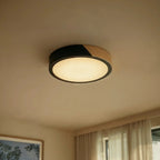Clérachic round flush ceiling light in black and wood, glowing warm in a curtained room at dusk.
