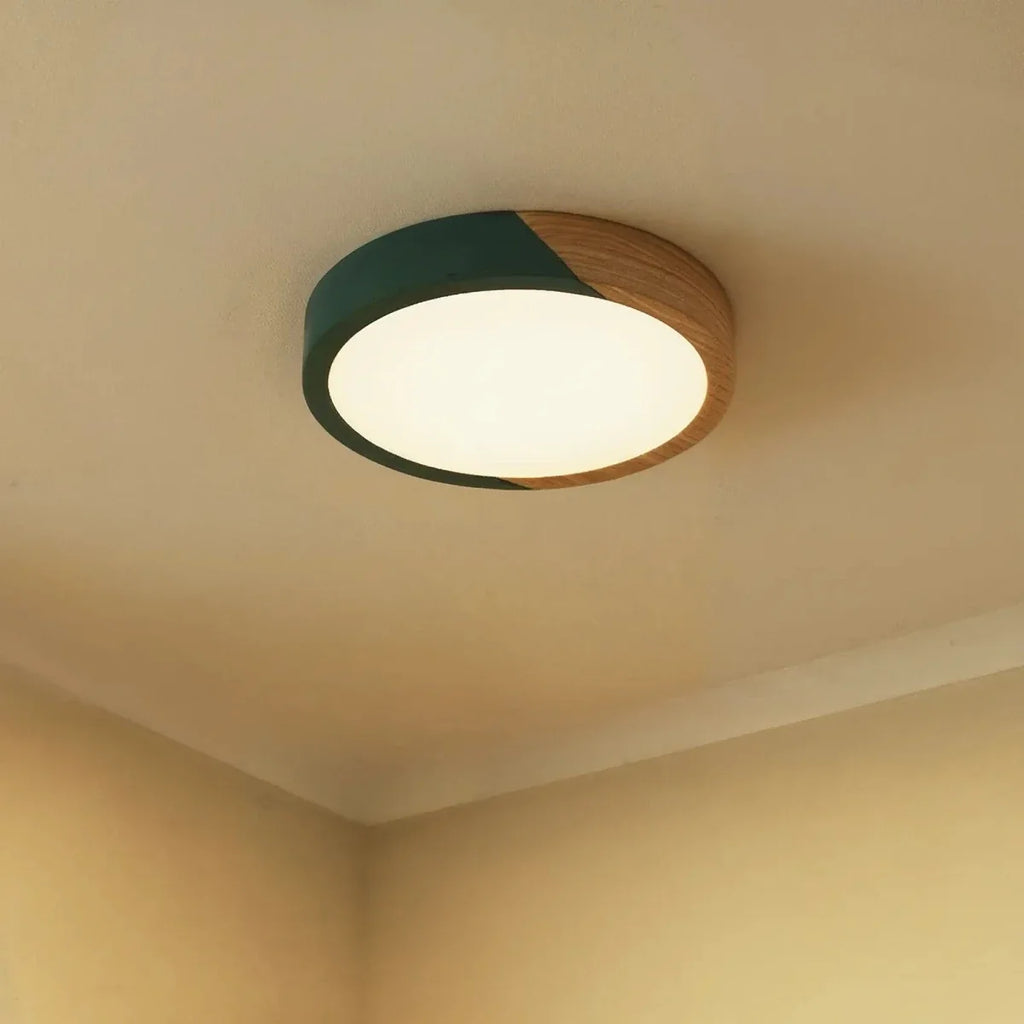 Clérachic round flush ceiling light in deep green and wood, glowing bright white in the corner of a softly lit room.