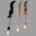 Three Clérachic squirrel and pinecone pendant lights in black, white and tan resin, each holding an exposed Edison bulb.